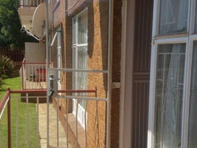 A functional balcony area featuring tiled flooring, a security gate, and metal railings, providing access to the apartment interior.
