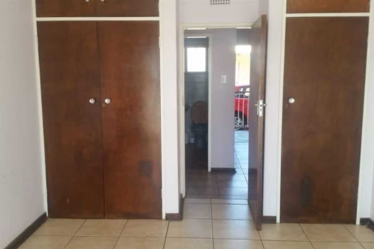 A vacant bedroom featuring built-in wooden cupboards and tiled flooring, with a view through to an adjacent bathroom area.