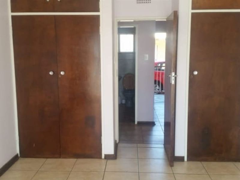 A vacant bedroom featuring built-in wooden cupboards and tiled flooring, with a view through to an adjacent bathroom area.