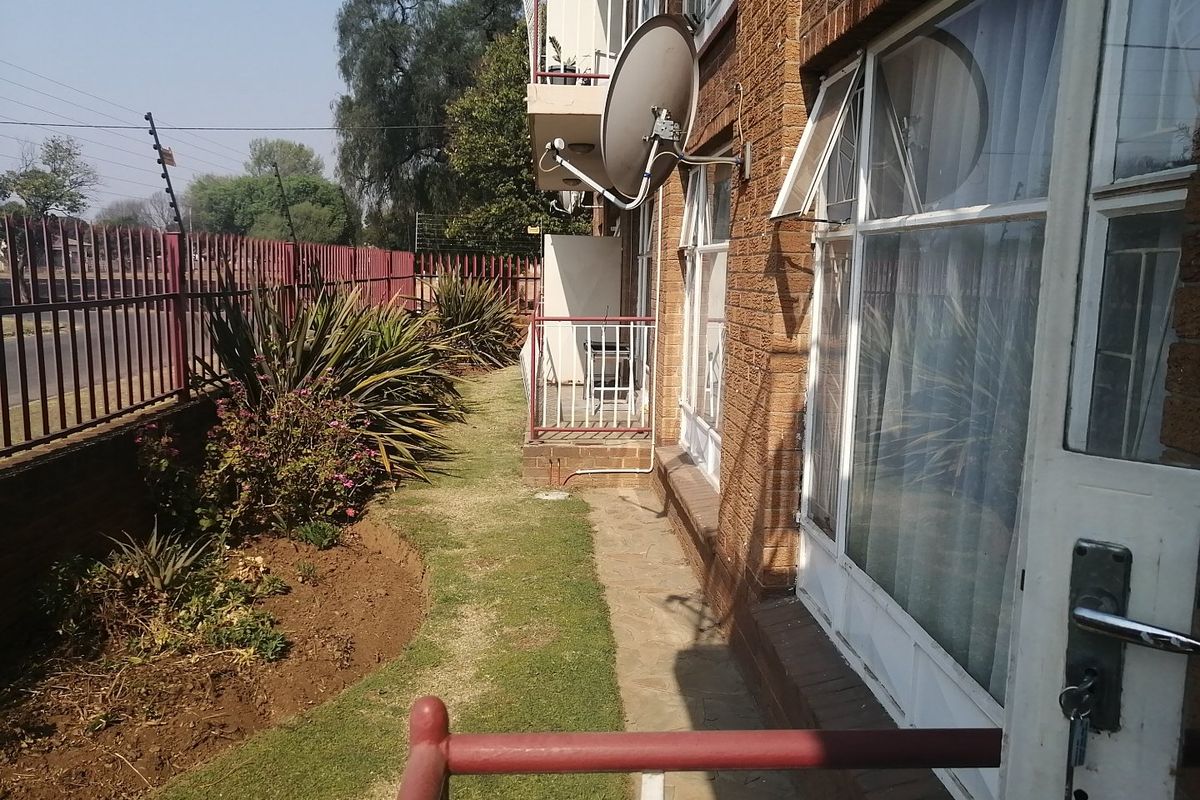 Exterior view of the apartment building featuring a brick facade, ground-level garden area, and metal security fencing.