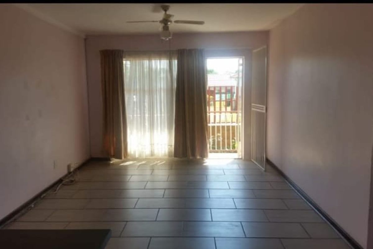An empty living room featuring tiled flooring, a ceiling fan, and a sliding glass door providing access to an outdoor area.