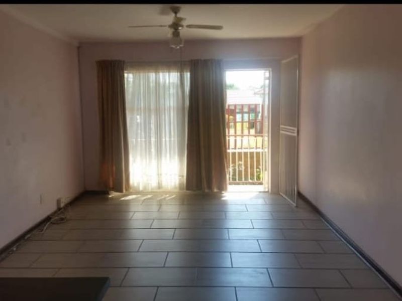 An empty living room featuring tiled flooring, a ceiling fan, and a sliding glass door providing access to an outdoor area.