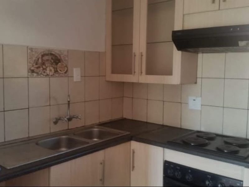 A functional kitchen featuring built-in cabinetry, a double sink, electric hob, oven, and extractor fan with a tiled backsplash.