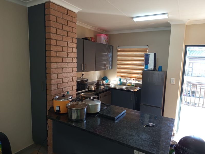 A functional kitchen featuring dark cabinetry, granite countertops, and a unique exposed brick pillar, with direct access to an adjacent balcony.