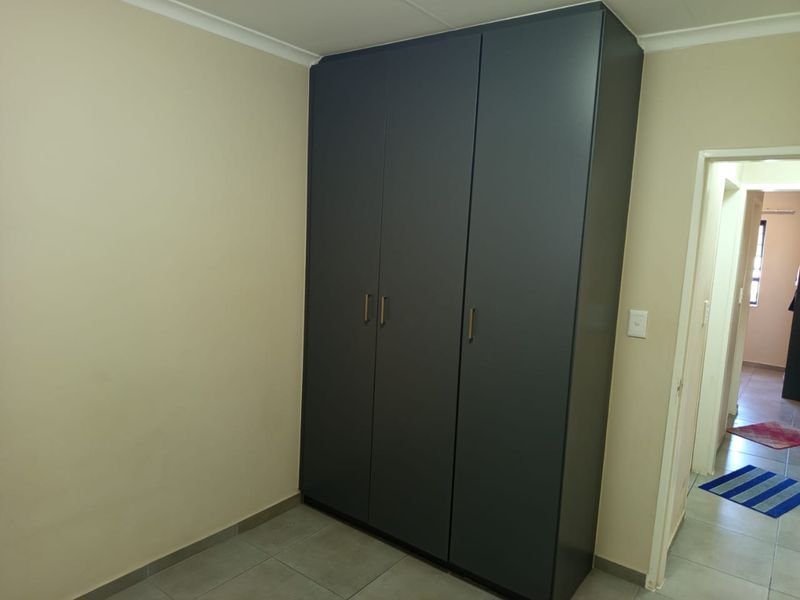 A clean, empty bedroom featuring modern dark grey built-in wardrobes and neutral tiled flooring.