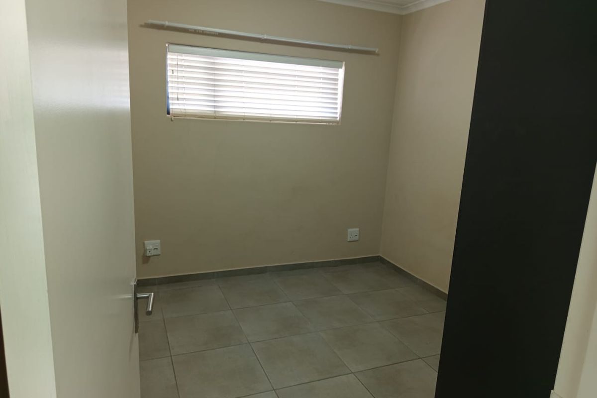 A clean, empty bedroom featuring neutral wall paint, tiled flooring, and a window fitted with venetian blinds.