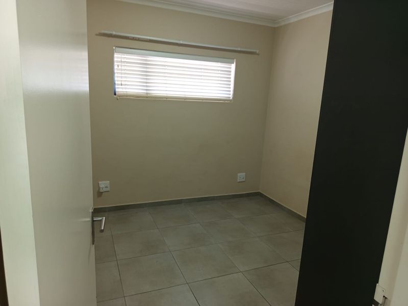 A clean, empty bedroom featuring neutral wall paint, tiled flooring, and a window fitted with venetian blinds.