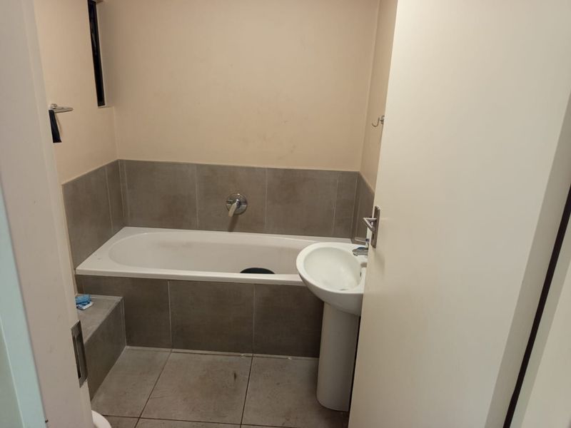 A functional bathroom featuring a built-in bathtub with tiled surround, a pedestal basin, and neutral floor tiling.