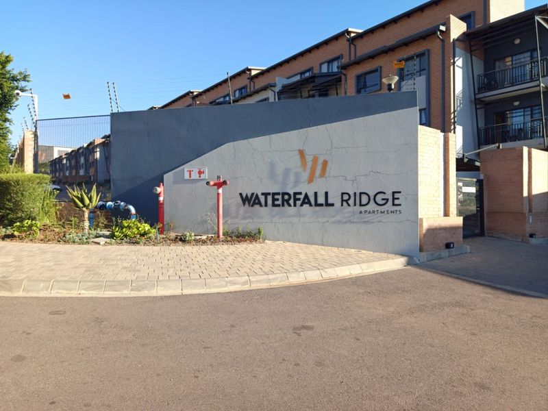 Entrance view of Waterfall Ridge Apartments featuring a paved driveway, brick building facade, and prominent complex signage.