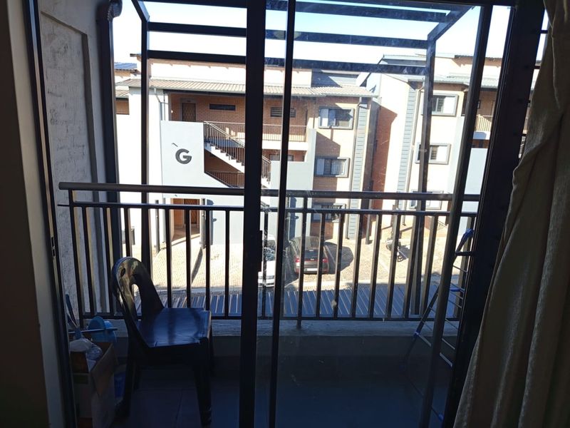 A balcony area featuring a metal balustrade and sliding glass door access, overlooking the apartment complex courtyard.
