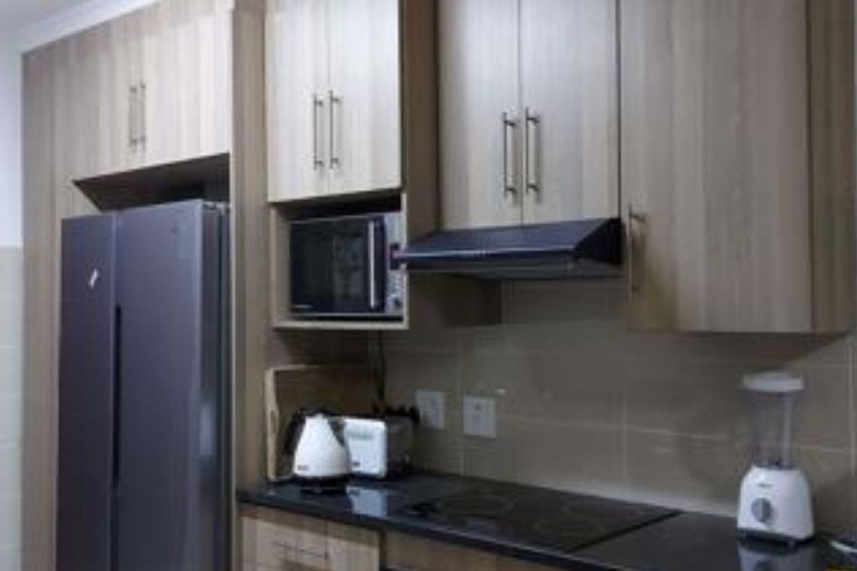 A functional kitchen featuring light wood-toned cabinetry, dark stone countertops, a built-in microwave, and an integrated extractor fan with a tiled backsplash.
