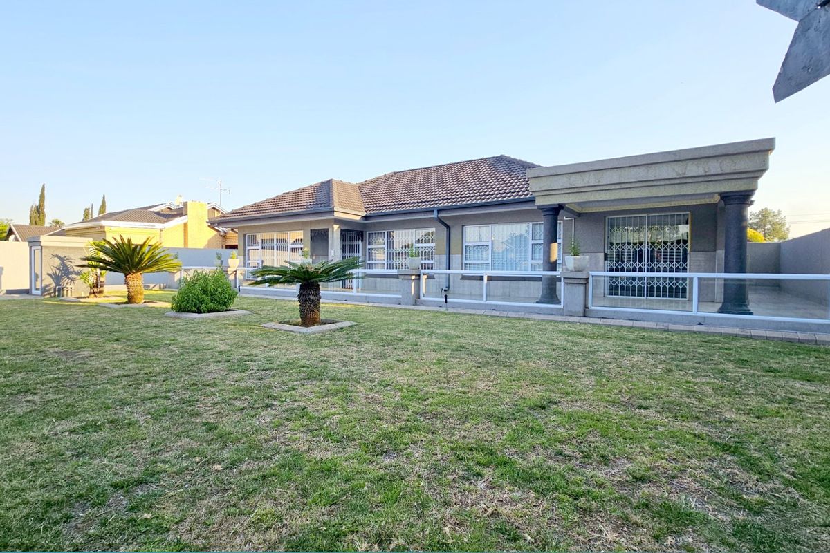 A well-maintained rear exterior view of the house featuring a spacious lawn, a covered patio area with concrete columns, and secure window treatments.