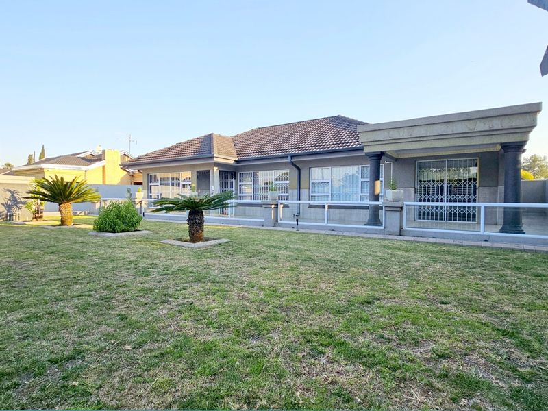 A well-maintained rear exterior view of the house featuring a spacious lawn, a covered patio area with concrete columns, and secure window treatments.