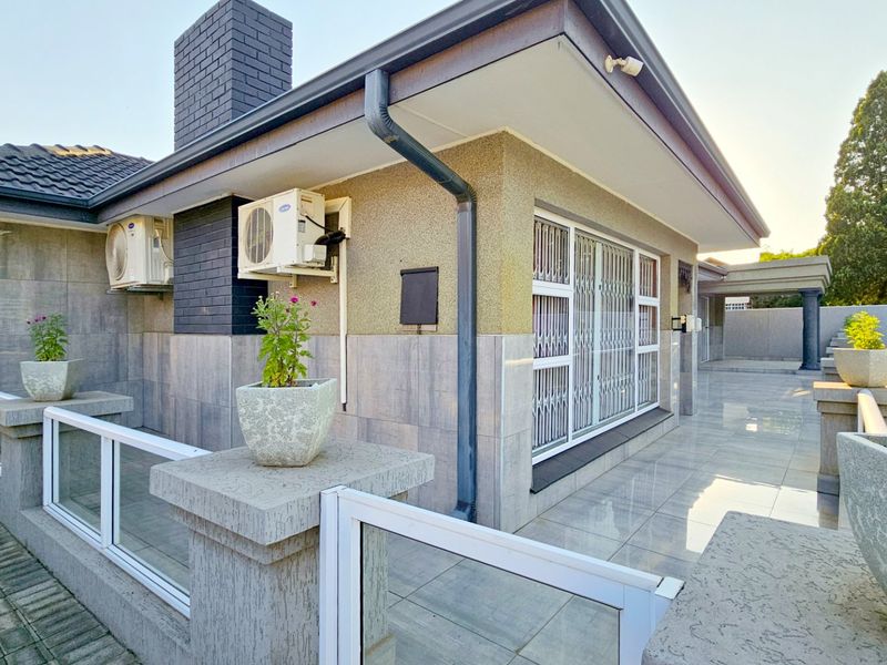 A well-maintained rear exterior view featuring a tiled patio area, brick chimney, and secure window treatments with integrated air conditioning units.