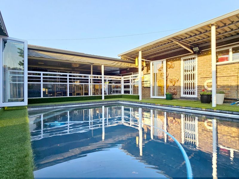 Outdoor pool area featuring a swimming pool, covered patio space with artificial turf, and brick exterior walls.