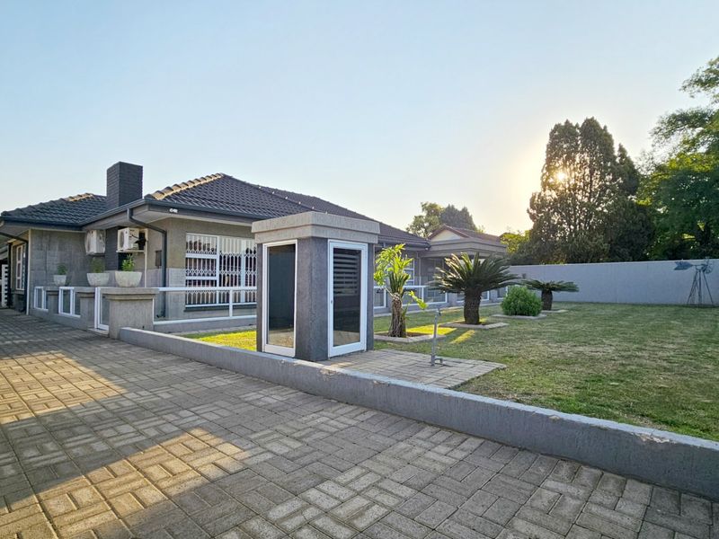 A well-maintained front exterior featuring a paved driveway, landscaped garden, perimeter wall, and secure access points with security bars.