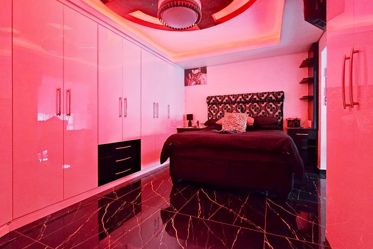 Modern bedroom featuring high-gloss built-in wardrobes, striking marble-effect flooring, and integrated ambient ceiling lighting.