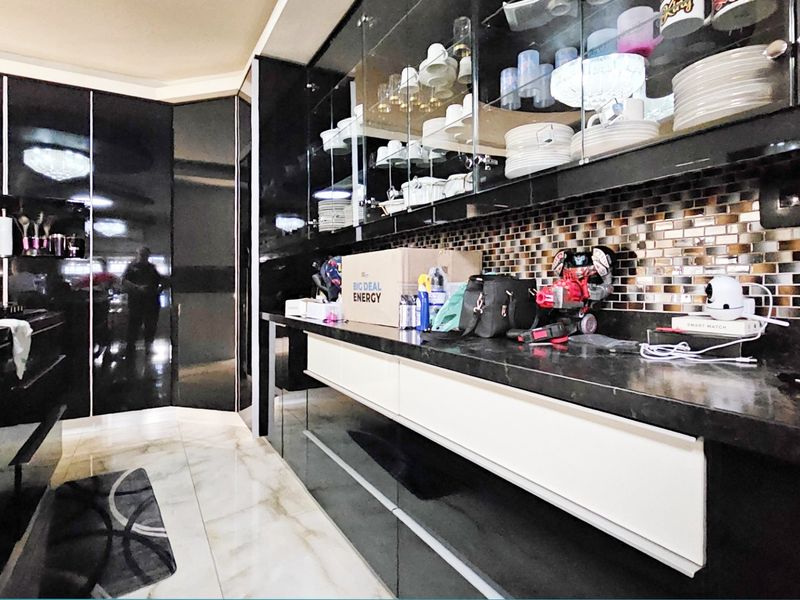 Modern kitchen featuring high-gloss black cabinetry, stone countertops, and a decorative mosaic tile backsplash with integrated glass-front display storage.