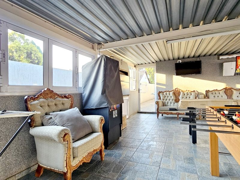 A covered outdoor patio area featuring tiled flooring, a corrugated metal roof, and a built-in braai, suitable for entertainment and relaxation.
