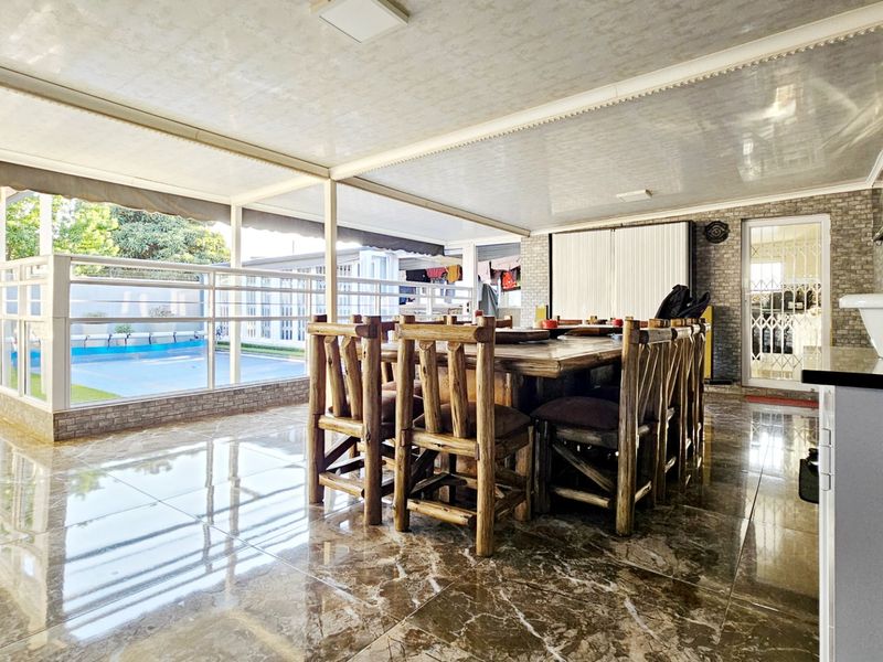 Spacious covered patio featuring polished tiled flooring, a brick feature wall, and direct access to the pool area, ideal for outdoor entertaining.