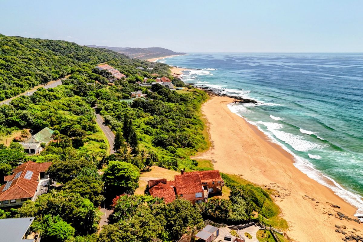 An aerial view of a coastal residential area featuring lush greenery, direct beach access, and proximity to the ocean.