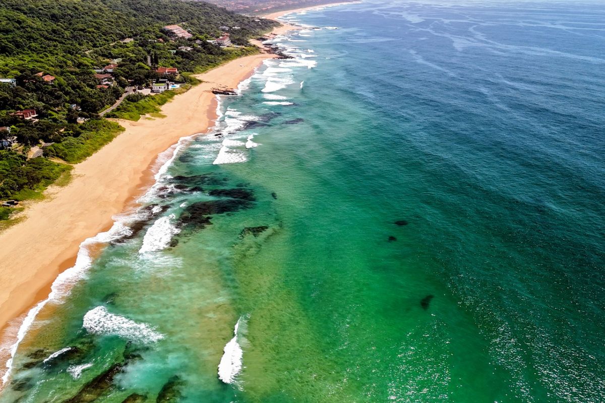 An aerial view of the coastal landscape, showcasing the sandy beach, turquoise ocean waters, and surrounding natural vegetation.
