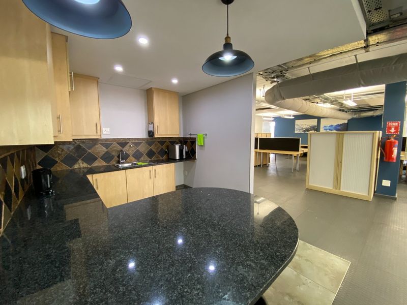 Open-plan commercial office space featuring a functional kitchenette with granite countertops, built-in cabinetry, and an exposed industrial ceiling design.