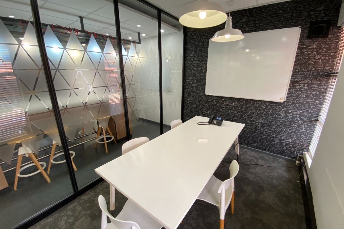 A modern commercial office meeting room featuring a glass partition wall, whiteboard, and contemporary pendant lighting.