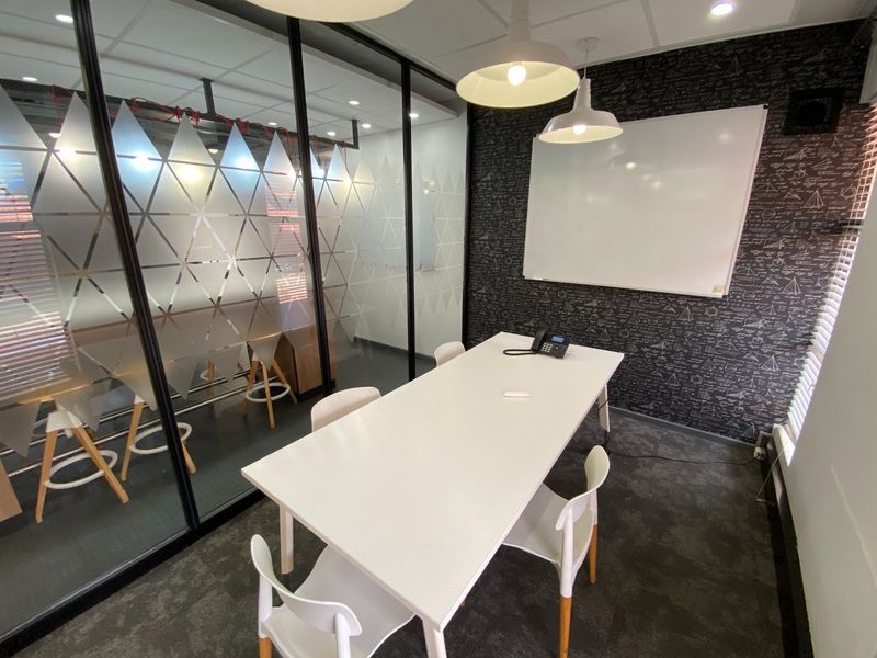 A modern commercial office meeting room featuring a glass partition wall, whiteboard, and contemporary pendant lighting.
