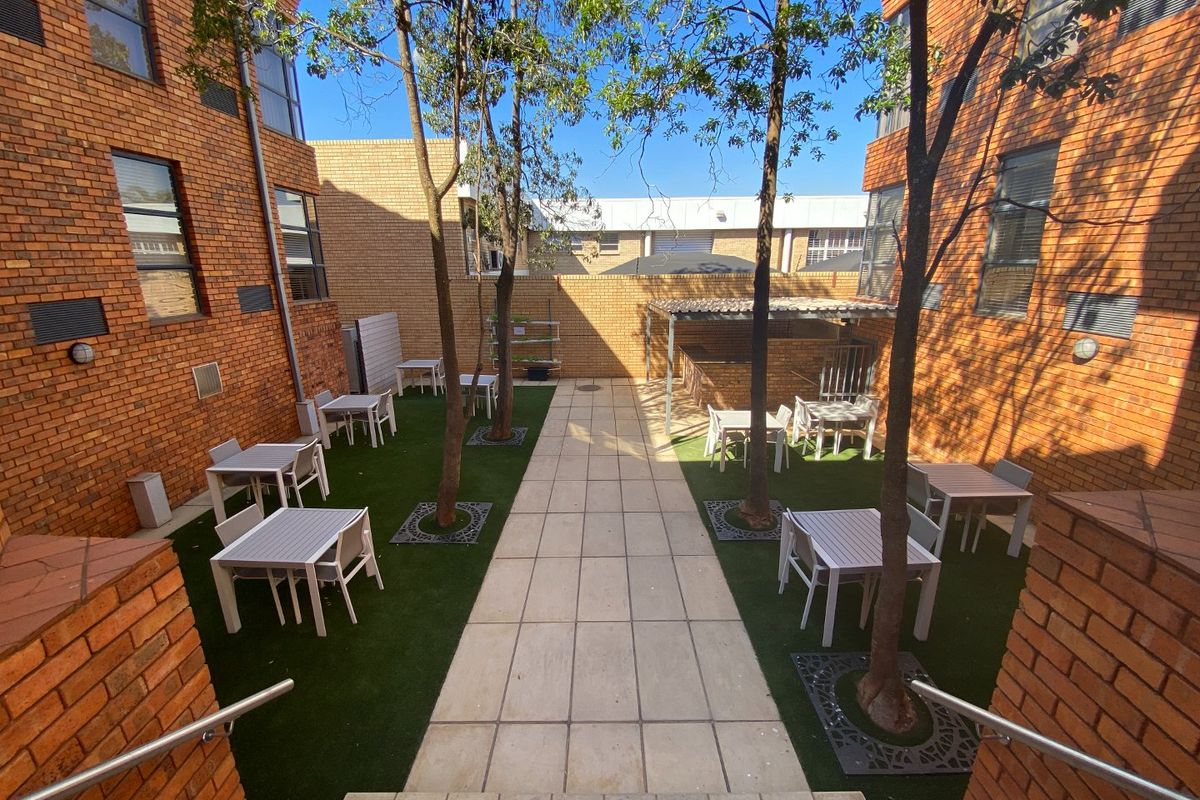 A well-maintained outdoor courtyard featuring a paved central walkway, artificial turf, brick facade walls, and a built-in brick braai area.