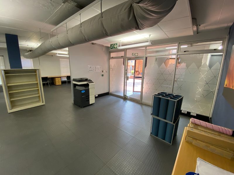 Open-plan commercial office space featuring exposed industrial ducting, durable rubber flooring, and glass partition walls with natural light access.