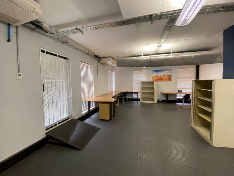 Open-plan commercial office space featuring industrial-style exposed cable trays, durable rubber flooring, and built-in desk configurations with security access.