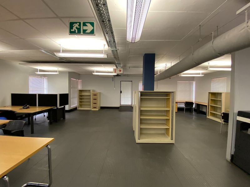 Open-plan commercial office space featuring industrial-style exposed ducting, suspended ceilings, and functional built-in storage units.
