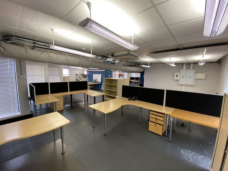 Open-plan commercial office space featuring suspended ceilings, exposed ducting, and integrated workstation partitions with natural light from large windows.