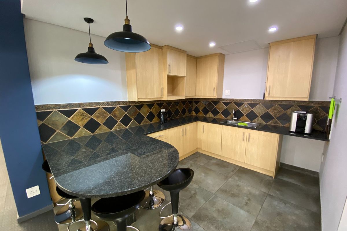 A functional kitchen featuring light wood cabinetry, dark granite countertops with an integrated breakfast bar, and a decorative tiled backsplash.