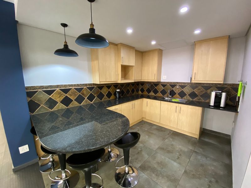 A functional kitchen featuring light wood cabinetry, dark granite countertops with an integrated breakfast bar, and a decorative tiled backsplash.