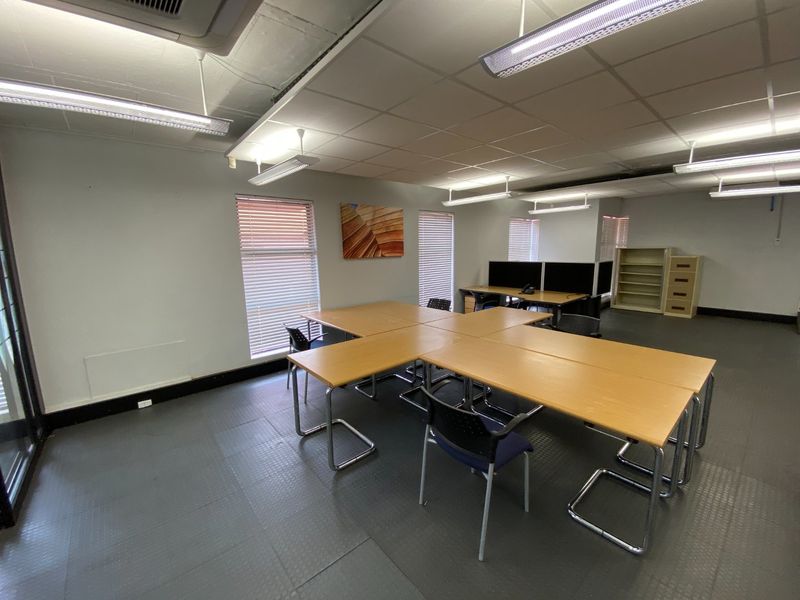 A functional commercial office space featuring suspended ceilings, durable rubber flooring, and large windows with venetian blinds for natural light control.