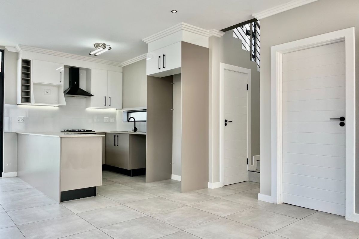 Modern open-plan kitchen featuring sleek cabinetry, a central island, gas hob, and high-quality tiled flooring, seamlessly integrated with the home's staircase and interior layout.