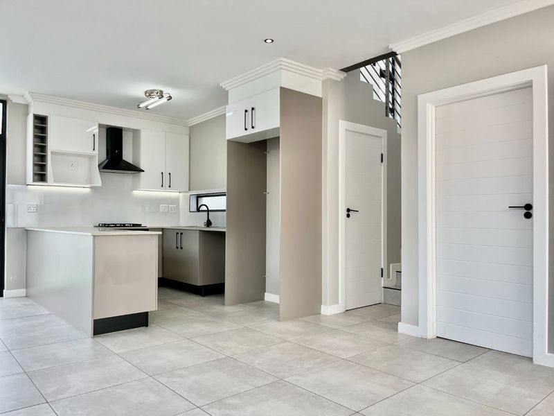 Modern open-plan kitchen featuring sleek cabinetry, a central island, gas hob, and high-quality tiled flooring, seamlessly integrated with the home's staircase and interior layout.