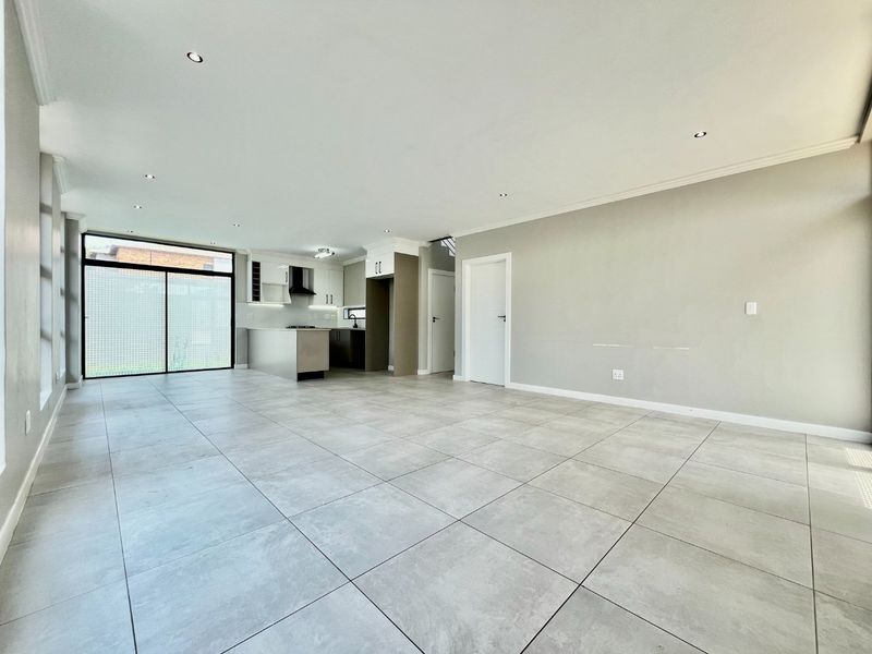 Spacious open-plan living area featuring large format floor tiles, recessed lighting, and a modern kitchen with built-in cabinetry and an extractor fan.