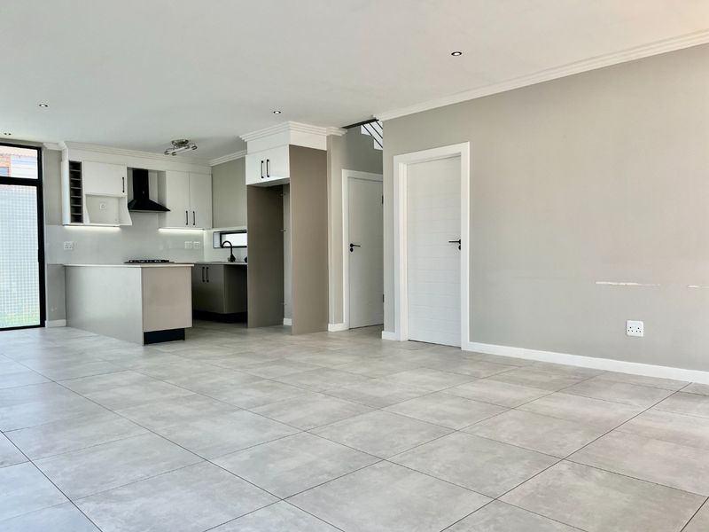 Modern open-plan living area featuring a sleek kitchen with built-in cabinetry, island, and neutral tiled flooring throughout.