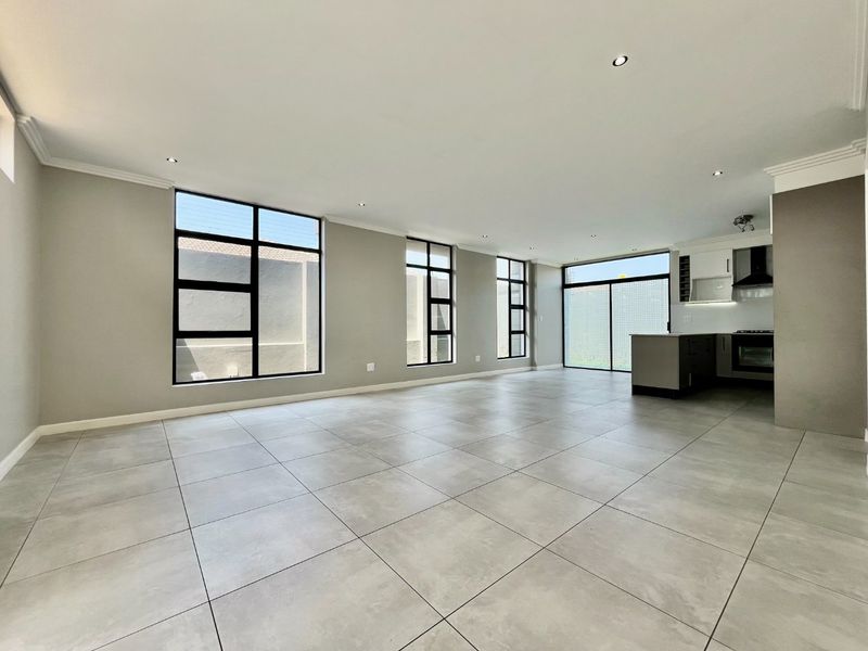 Spacious open-plan living area featuring large windows, modern tiled flooring, recessed lighting, and a sleek kitchen with built-in appliances.
