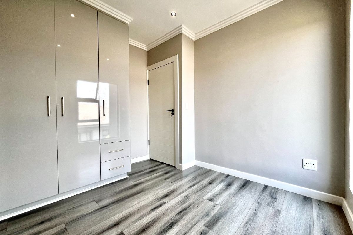 A bright, modern bedroom featuring high-gloss built-in cupboards, contemporary laminate flooring, and clean neutral finishes throughout.
