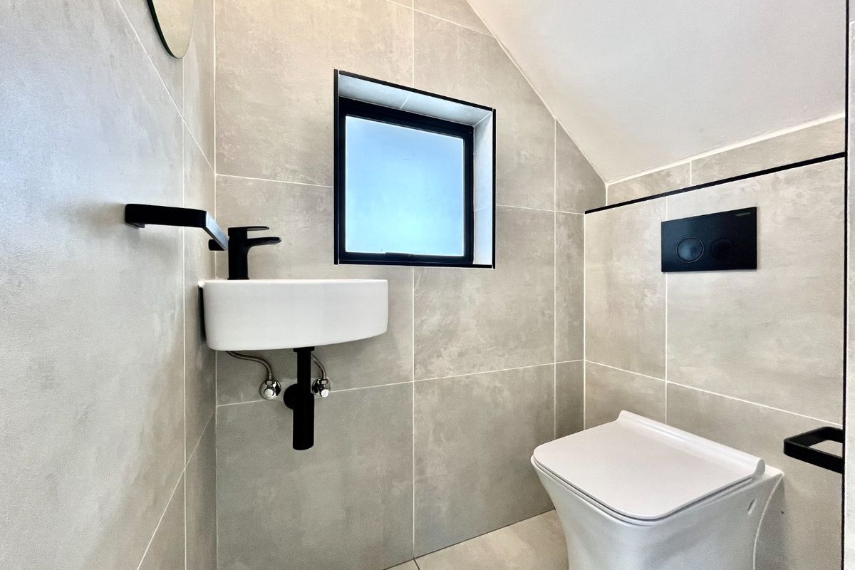 Modern guest bathroom featuring large format grey tiles, a wall-mounted basin with black fixtures, and a sleek wall-hung toilet with a concealed cistern.
