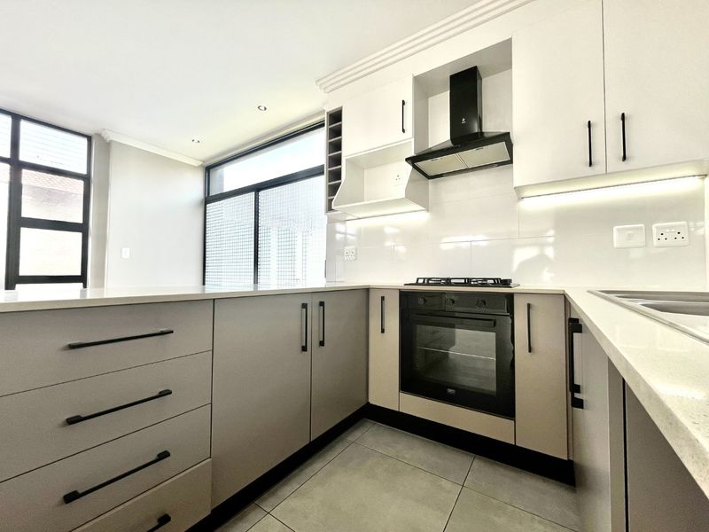 Modern kitchen featuring sleek built-in cabinetry, stone countertops, integrated oven, gas hob, and extractor fan with ample natural light.