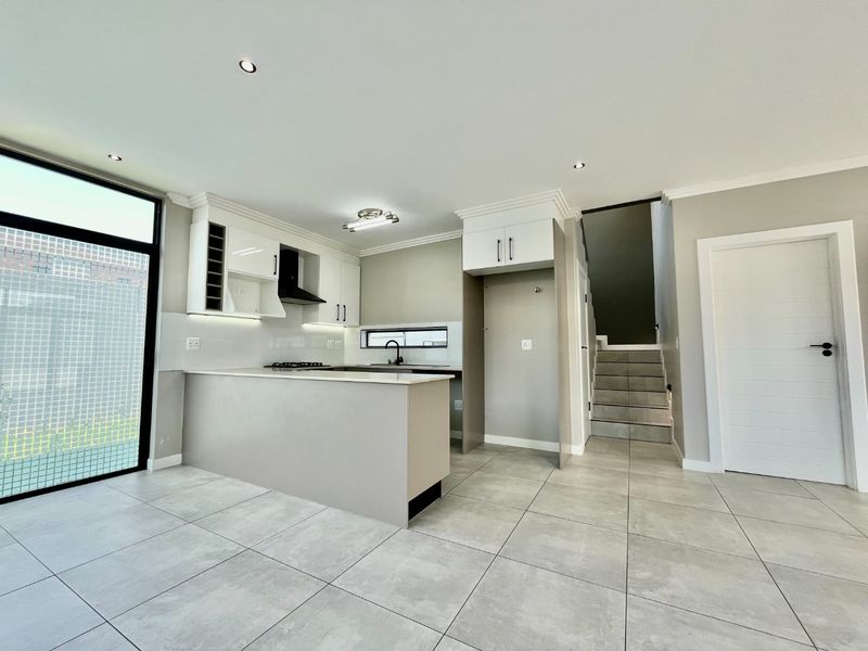 Modern open-plan kitchen featuring sleek cabinetry, gas hob, and tiled flooring, seamlessly integrated with a staircase and access to outdoor space.