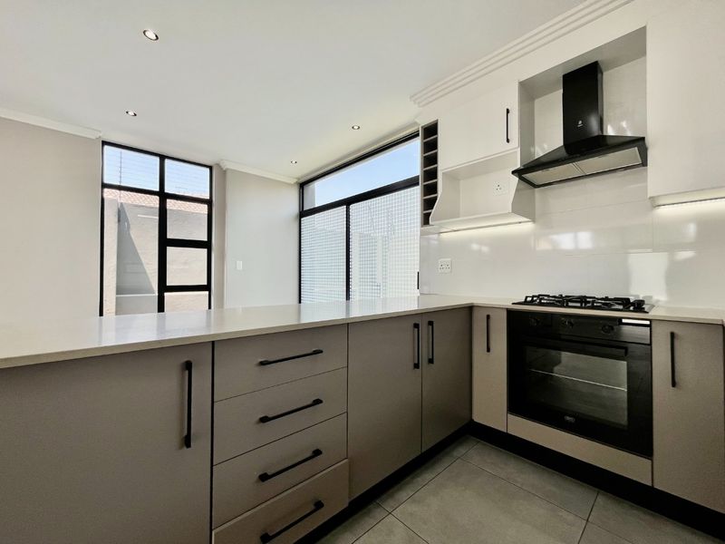 Modern kitchen featuring sleek cabinetry, stone countertops, integrated gas hob, built-in oven, and extractor fan, complemented by large windows and contemporary tiled flooring.