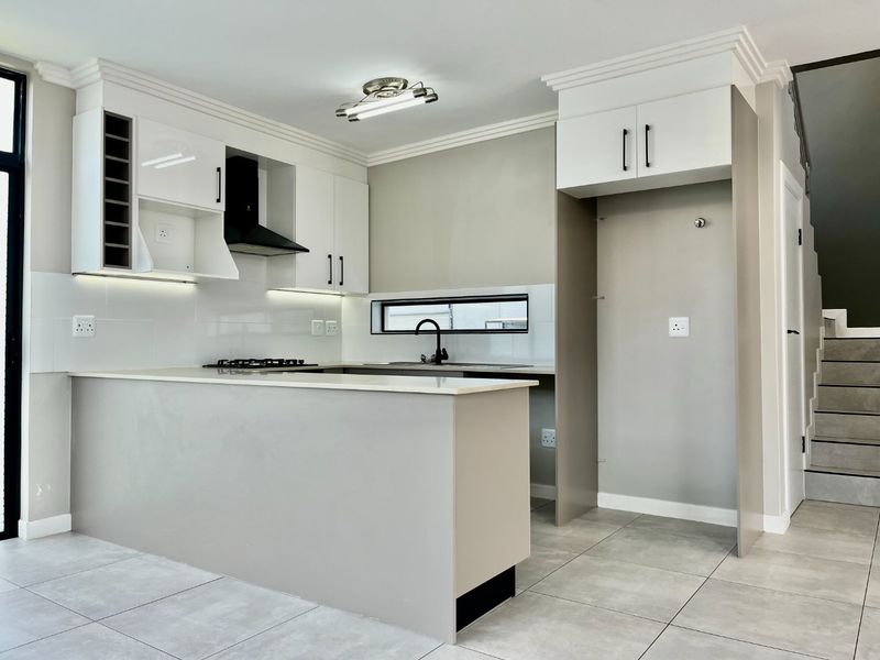Modern kitchen featuring sleek white cabinetry, stone countertops, a gas hob with extractor, and tiled flooring in a clean, contemporary open-plan layout.