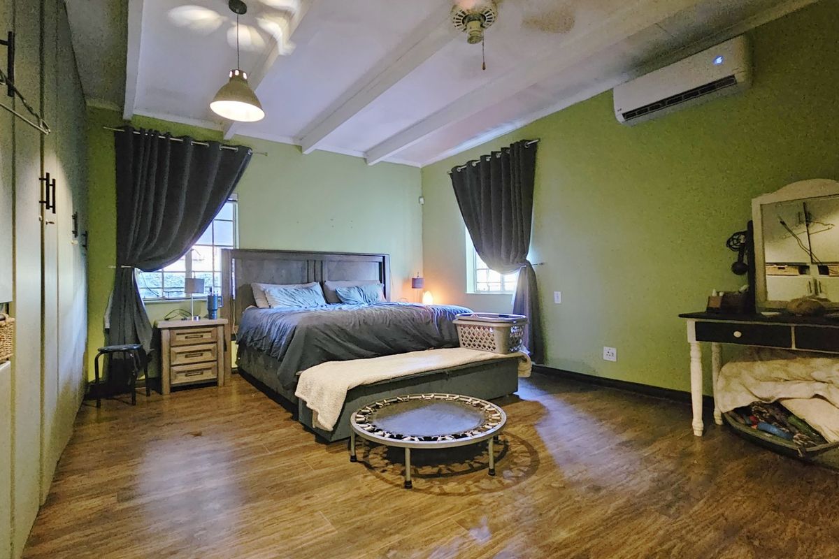 Spacious bedroom featuring laminate flooring, exposed ceiling beams, built-in cupboards, and a wall-mounted air conditioning unit.