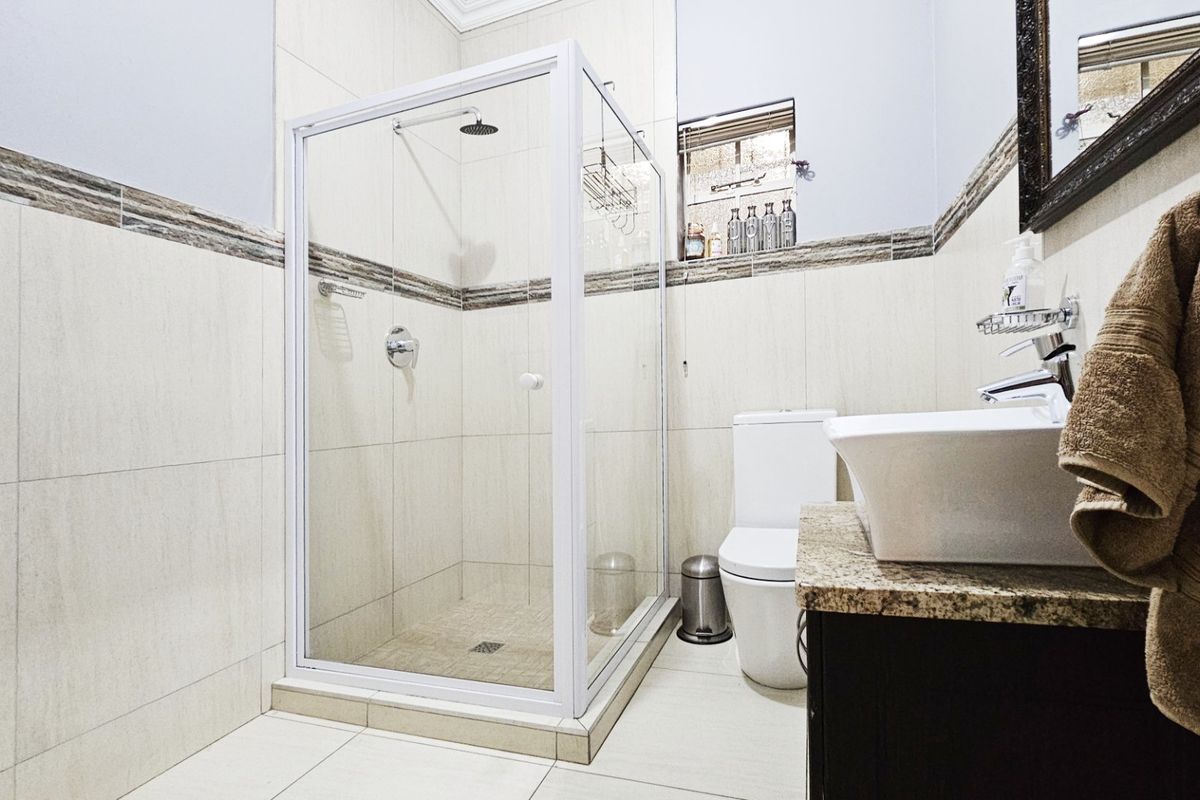 A well-maintained bathroom featuring a glass-enclosed shower, a modern basin with a granite countertop vanity, and neutral wall and floor tiling.